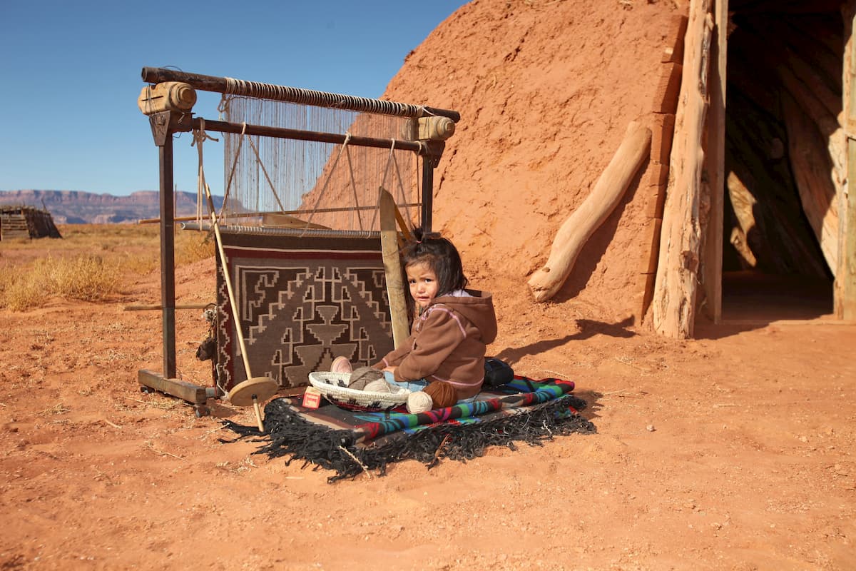 Navajo Child Sitting Next to Traditional Rug Making Tools