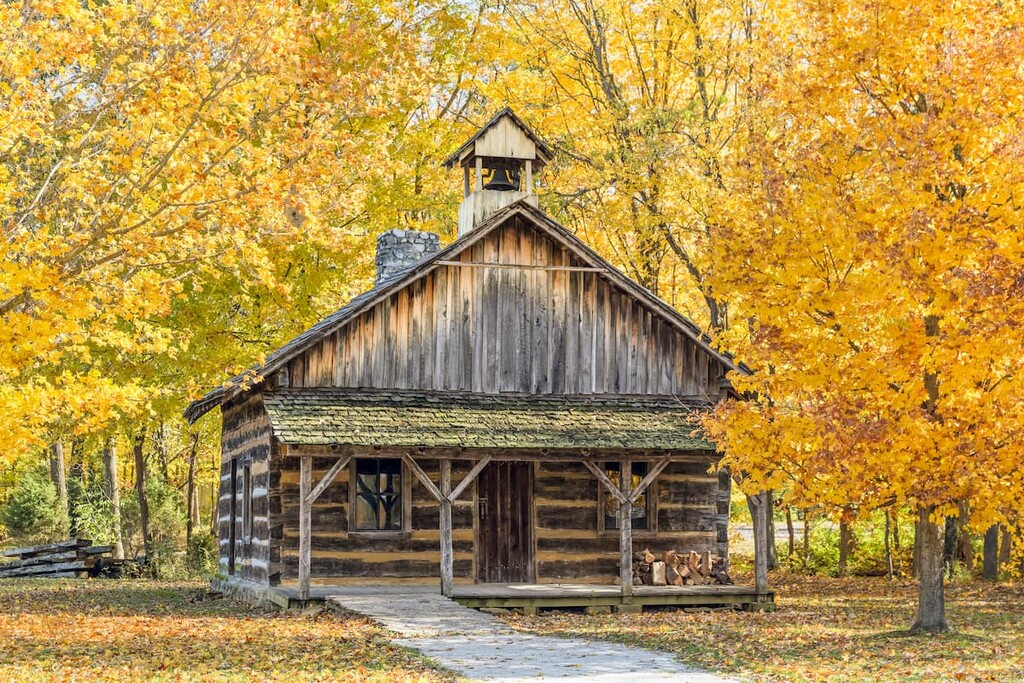 A log church is surrounded by colorful autumn trees in an Indiana