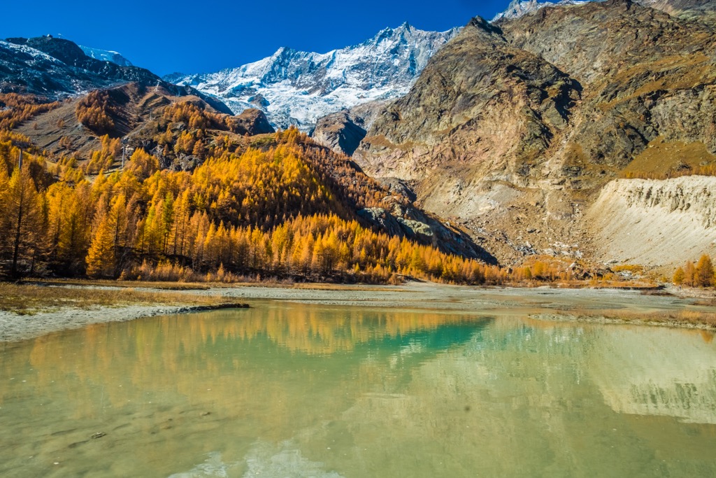 Goldener Lärchenwald über einem Gletschersee im Saastal, Wallis