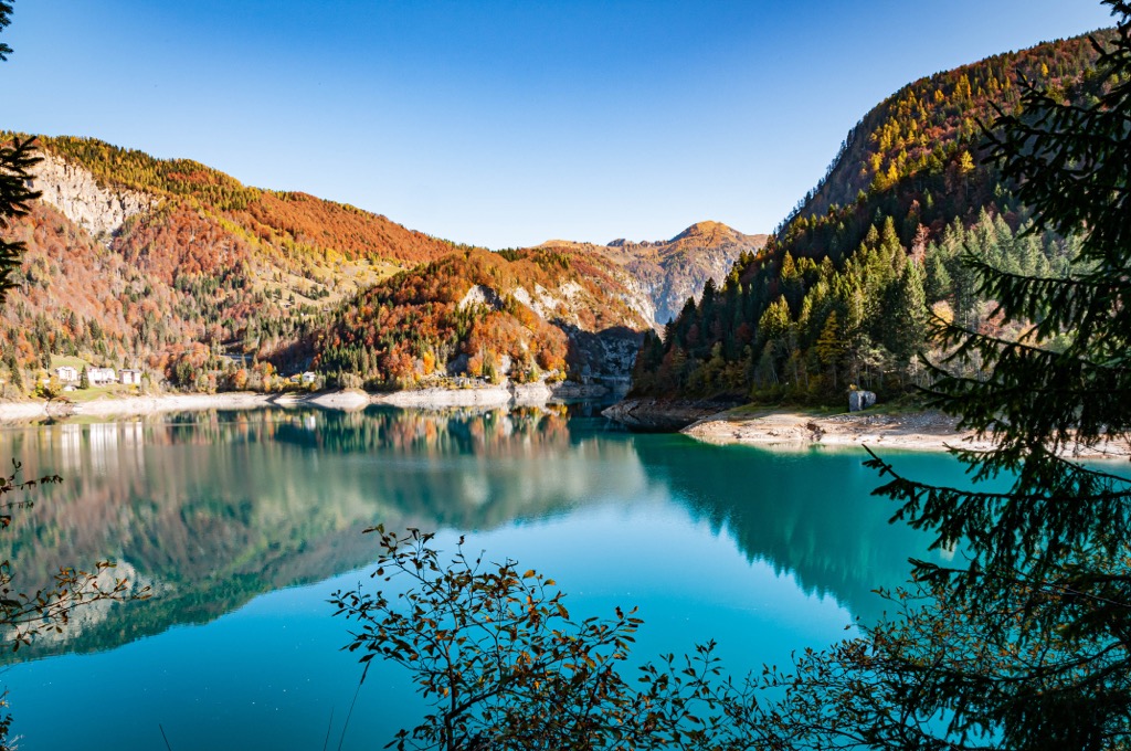 Lago di Sauris im Herbst, Karnien, Friaul, mit türkisfarbenem Wasser und gold- und rostfarbenen Hängen