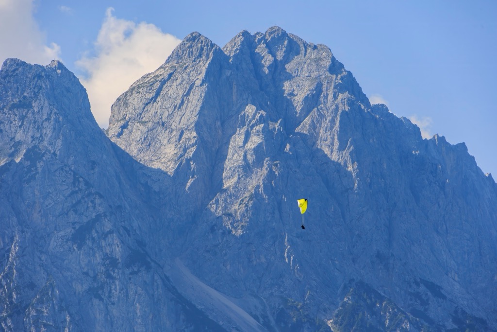 A paraglider soars across the towering limestone walls of the Zugspitze massif. Wetterstein