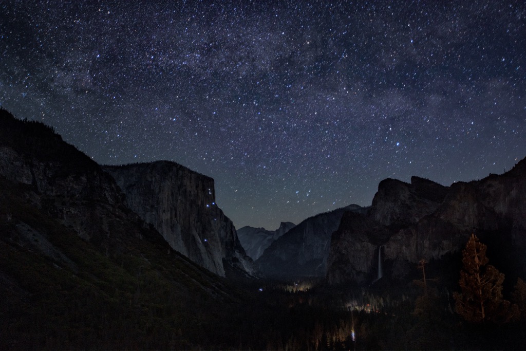 An extended exposure photo of Yosemite at night shows the stars and Milky Way, but also the climbers’ headlamps up on El Capitan